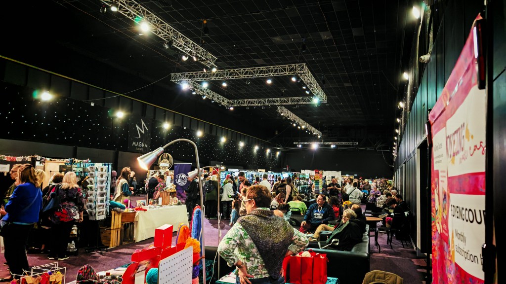 A photo taken at The Wool Monty 2025, with lots of people milling around in aisles, sitting and chatting and browsing stands